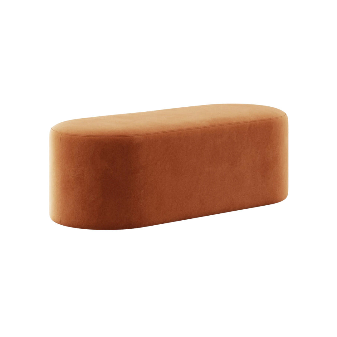 An elongated orange oval pouf upholstered in premium velvet in a rich, earthy tone, presented without any visible legs.